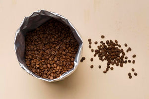 Dark roast coffee beans spilling out of a burlap bag, showcasing their rich, deep brown color and oily surface.